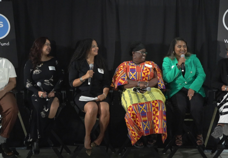 A group of 6 women sitting on tall stools, speaking at a panel discussion