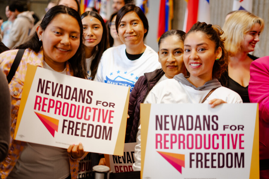 Group of women with dark hair. Two women hold signs that say Nevadans for Reproductive Freedom