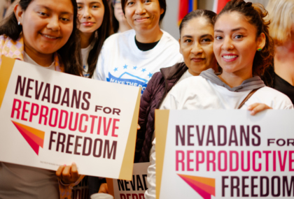 Group of women with dark hair. Two women hold signs that say Nevadans for Reproductive Freedom