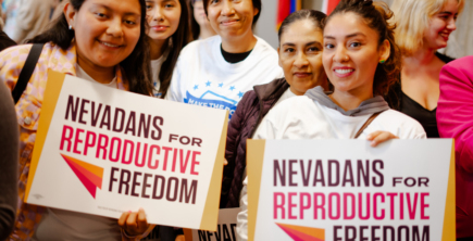 A group of Latine women, two holding signs that say 'Nevadans for Reproductive Freedom.' Photo credit: Nevadans for Reproductive Freedom, a Tides Healthy Democracy Fund