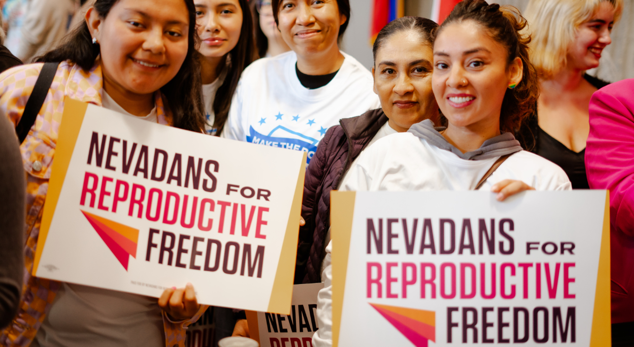 Group of women with dark hair. Two women hold signs that say Nevadans for Reproductive Freedom