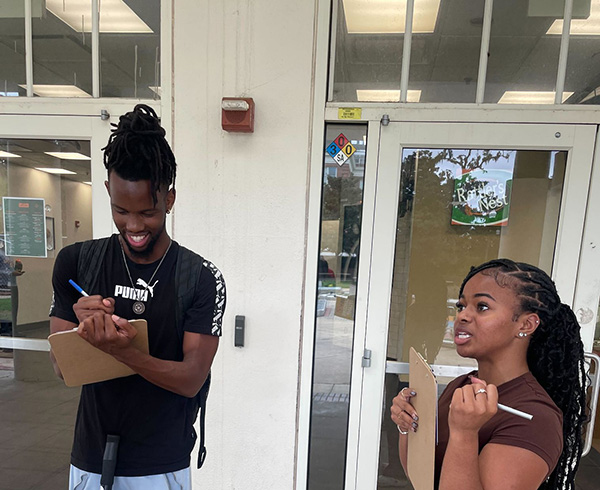 A man and a woman with dark skin holding clipboards