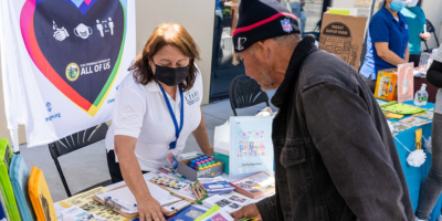 A woman at a table at an outdoor event shows a man some brochures.