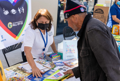 A woman at a table at an outdoor event shows a man some brochures. Photo credit: Nuestra Casa, a Victor & Lorraine Honig Initiative grantee partner